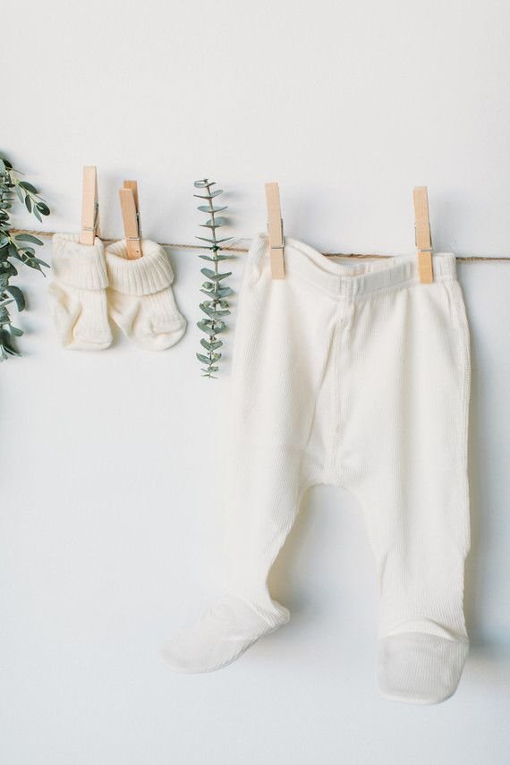 Pantalón junto con guantes de bebé colgados con pinzas de madera en una cuerda que contiene hojas.