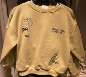 Sudadera amarilla Strong Swell para niño: sudadera de cuello redondo con estampado de palmeras y estilo surfero sobre fondo blanco.